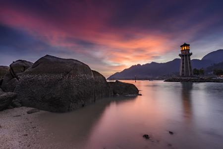 Colorful sunset with rocky coastline in foreground and lighthouse in backgroundの写真素材