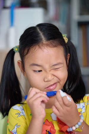 The girl happily drawing and painting on white paper. Asian girl sitting intently doing artwork on children's table.の写真素材