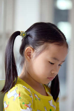 The girl happily drawing and painting on white paper. Asian girl sitting intently doing artwork on children's table.の写真素材