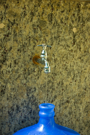 Water Tap dropping just a little bit of water to fill the big blue bottleの写真素材