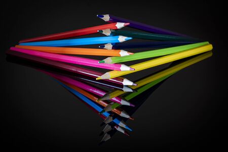 Colored upright crayons of different colors reflected on a black background