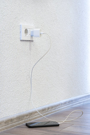 A charger in the socket that charges a mobile phone that stands on the floorの写真素材