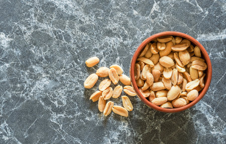 Peanuts in a bowl scattered next to it on a marble surface