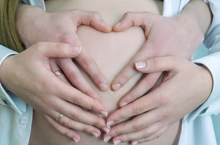 Four hands on a pregnant belly, close-up, Heart Shaped Pregnancy Portrait