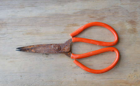 old rusty scissor with red plastic handle on wooden board