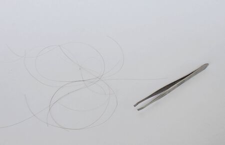 silver tweezers and hair on white background