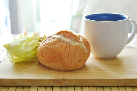 bun filled tuna mayonnaise and lettuce with coffee cup on wooden chop block