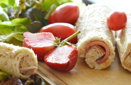 bread stuffed pork bologna roll with cut strawberry and vegetable on wooden chop blockの写真素材
