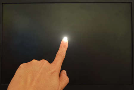 human finger touching on black computer screen and light on