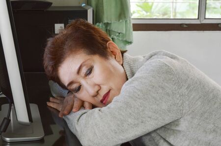 Asian elder woman take a nap on desk in front of personal computerの写真素材