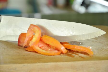tomato slicing by knife on wooden chop block