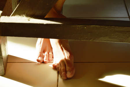 foot and leg on tile floor under wooden table in homeの写真素材