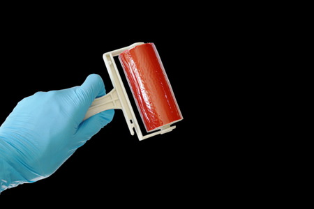 hand in blue rubber glove holding red sticky dust roller on black backgroundの写真素材