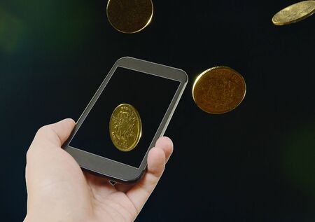 Hand holding smart phone and gold coin floatingの写真素材