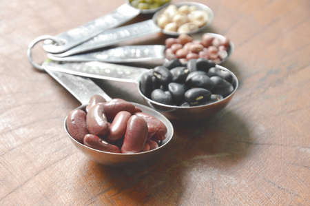 raw variety bean and cereal plant in measuring spoon on wooden table