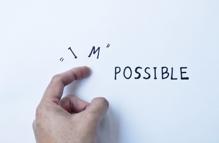 human finger poking impossible to possible words on white paper background