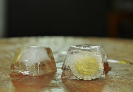 coin freezing in ice cube on wooden boardの写真素材