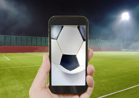mobile phone showing football on screen in stadium background
