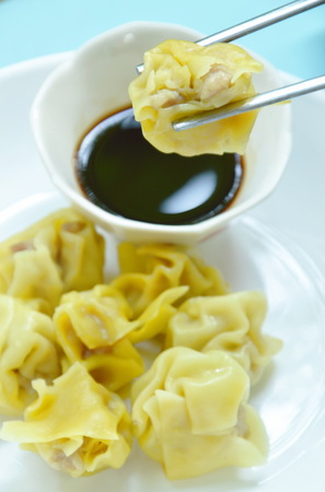 Chinese pork dumpling picking in stainless chopsticks on soy sauce cupの写真素材