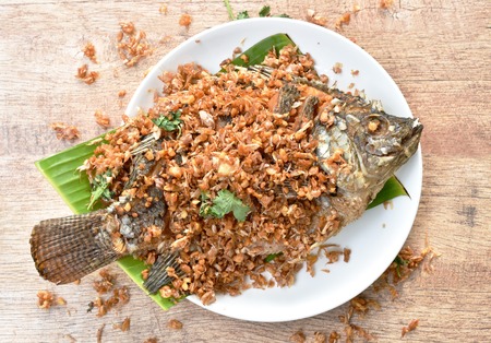 Batter fried mango fish topping chop garlic on banana leaf