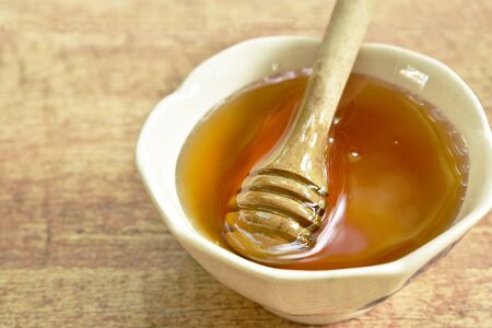 honey and wooden scoop in cup on tableの写真素材