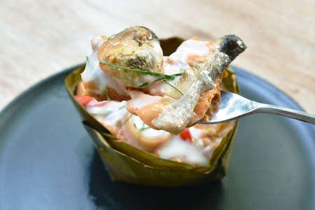 fork scooping steamed curry salmon fish with squid and mussel wrapped in banana leafの写真素材