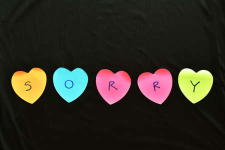 colorful sticky paper note with hearth shape write sorry on black fabric background