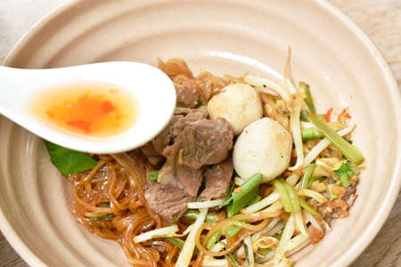 rice noodles topping braised pork and ball on bowl with bone in brown herb soup cup