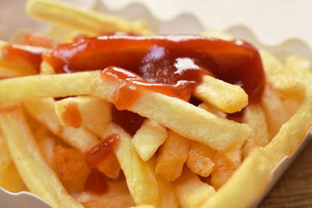 French fries mixed with salt in paper box dipping ketchup on tableの写真素材