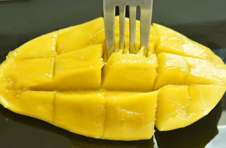 mango tropical fruit slice dice shape stabbing by silver fork on plateの写真素材