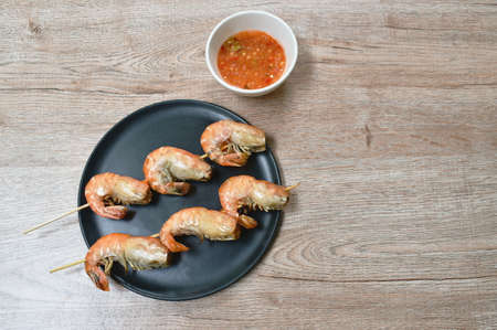 grilled shrimp with salt stabbing wooden stick on plate dipping spicy chili sauce