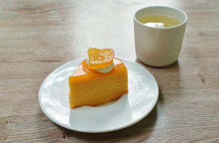 orange cake with cream topping fruit and hot tea cup on tableの写真素材