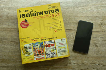 Bangkok Thailand September 19, 2021 : Thailand yellow pages book obsolete method for searching telephone number and address with smartphone on tableのeditorial素材