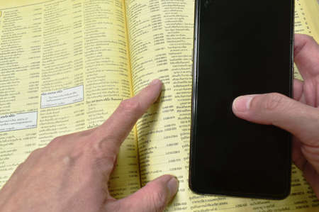 Bangkok Thailand September 19, 2021 : Thailand yellow pages book obsolete method for searching telephone number and address with smartphone on tableのeditorial素材