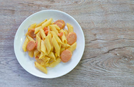 stir fried penne Italian pasta with slice pork sausage and garden pea with corn in ketchup on plateの写真素材