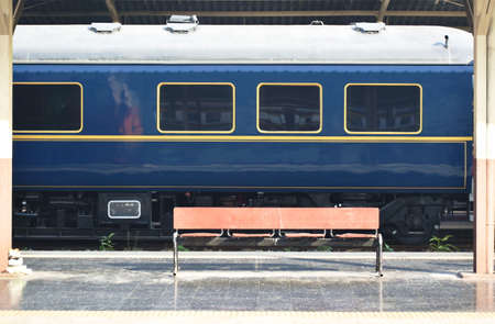 wooden bench for passenger waiting with blue train parking background in railway station platform