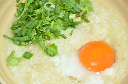 rice porridge mashed pork with chop spring onion and parsley topping egg yolk on bowlの写真素材