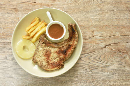 grilled pork chop steak with french fries and slice pineapple dipping gravy sauce on plateの写真素材