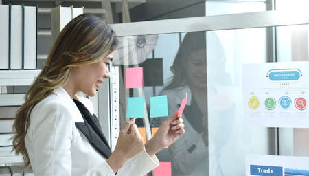 happy  busimess Asian woman looking at paper note stick on glass board with success moment in office