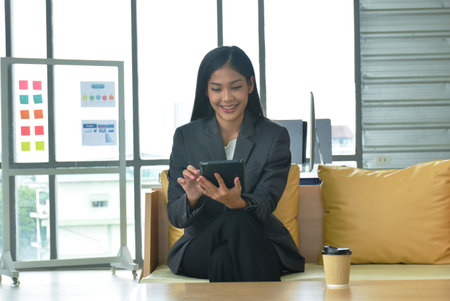 happy busimess Asian woman looking at mobile phone for relaxing after work in officeの写真素材