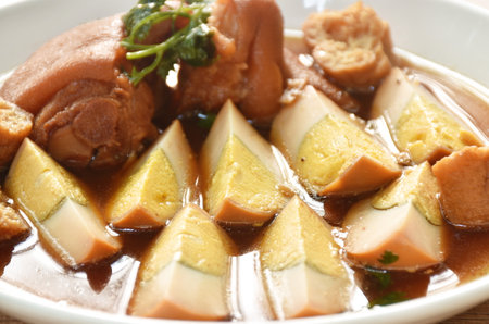 boiled half cut egg with tofu in herb brown soup and pork leg on plateの写真素材