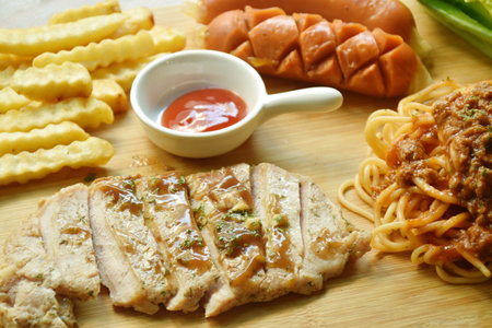 grilled pork steak dressing gravy sauce with French fries and cos lettuce salad couple sausage on chopping blockの写真素材