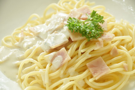 steamed spaghetti white cabonara cream sauce topping slice ham pork on plateの写真素材