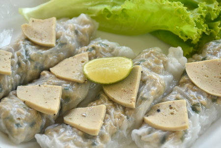 Vietnamese steamed rice dumpling stuffed chop pork and topping slice sausage with fresh green lettuce salad on plate dipping sweet chili sauce dressing crispy fried shallot in cupの写真素材