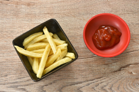 French fries mixed with salt in cup dipping ketchup on table