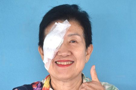 elder woman covering protection on right eye smiling after cataract surgery in blue backgroundの写真素材