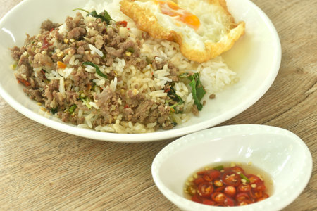 spicy stir fried chop beef meat with basil leaf and chili on rice topping egg in plate dressing fish sauceの写真素材