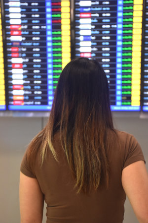 Asian woman carrying travel bag and look at airline schedule board in airportの写真素材