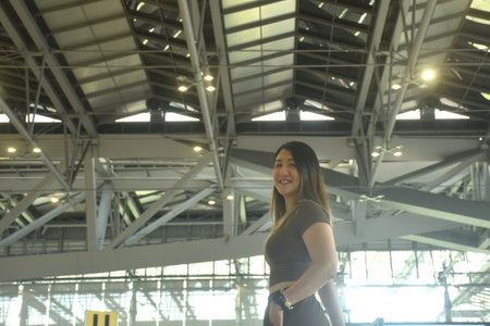 Asian woman smiling while carrying travel bag in airportの写真素材