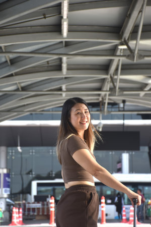 Asian woman smiling while carrying travel bag in airportの写真素材